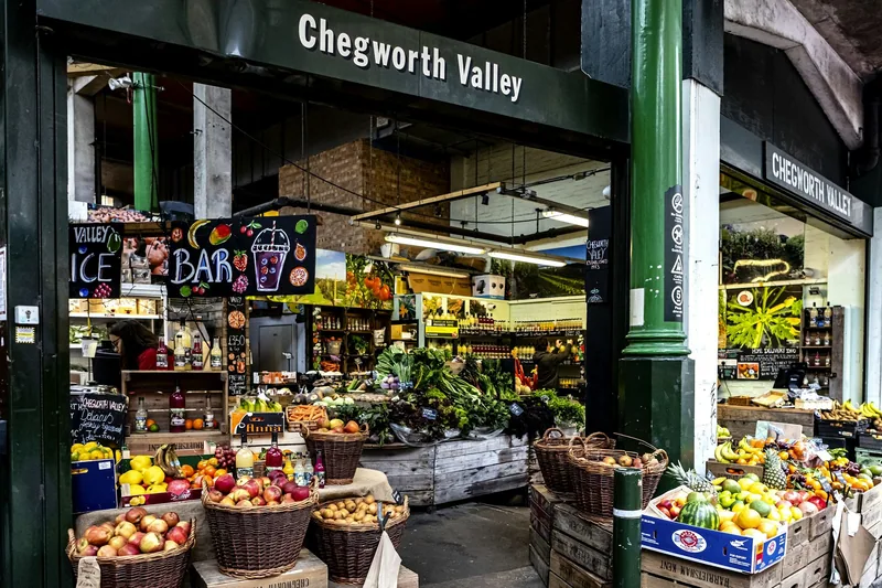 Frukt- og grønnsaksbod på Borough Market med kurver fulle av epler, sitroner og friske grønnsaker