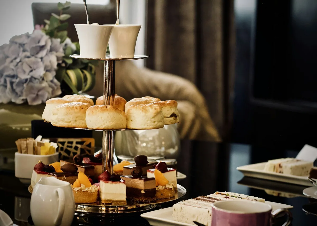 Etasjefat med scones, små kaker og sandwicher til afternoon tea, med krem i skåler på toppen