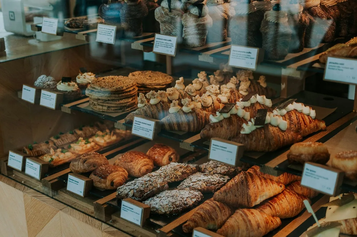 Glassdisk i et bakeri med croissanter, mandelcroissanter, pain au chocolat og kaker på hyller med små prislapper