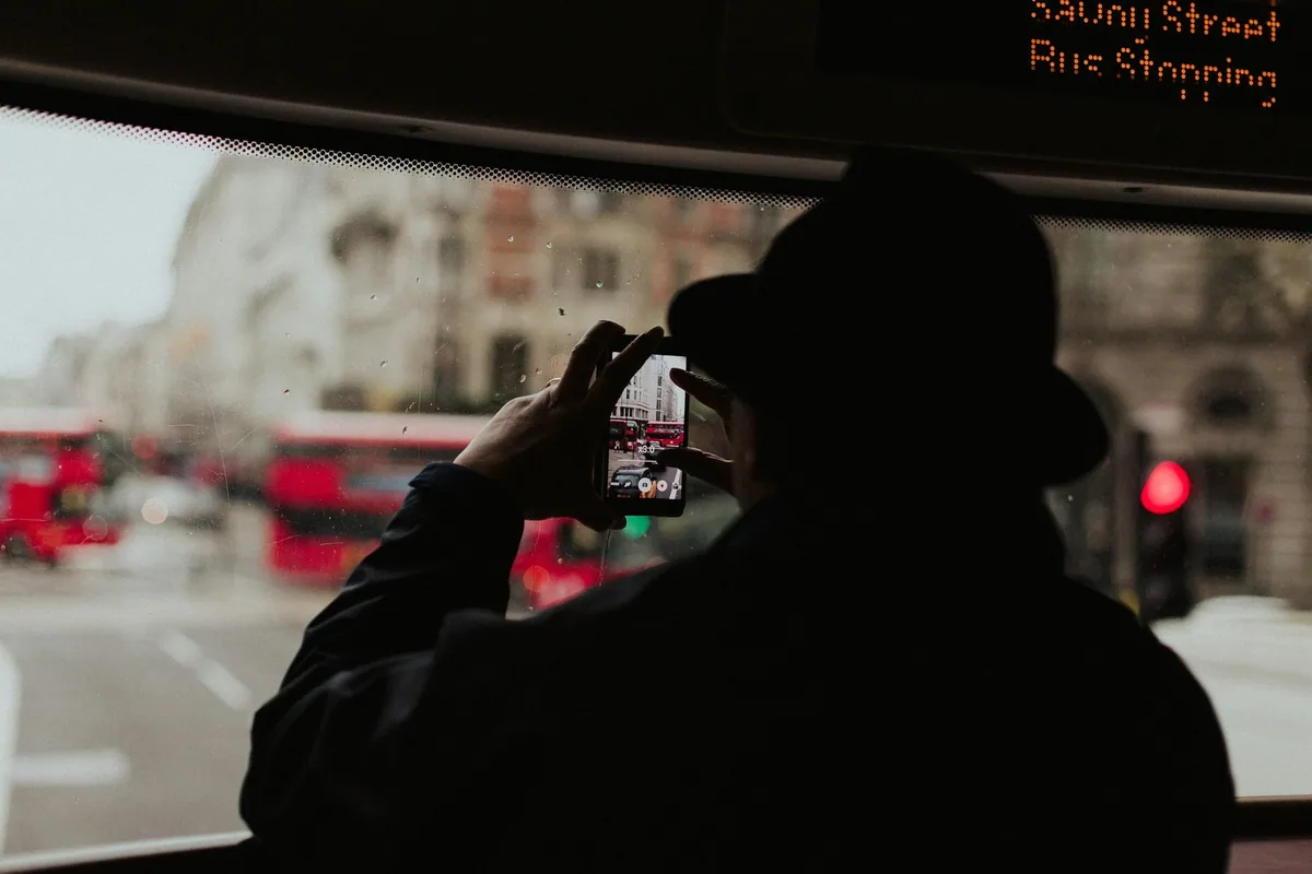 Passasjer i silhuett filmer gaten med mobilen fra bussvinduet, med røde busser utenfor og stoppskjerm i taket