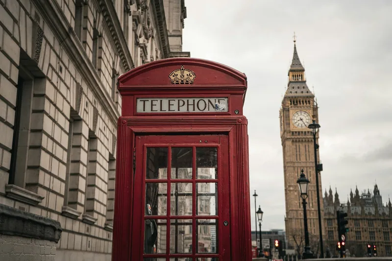 Rød telefonkiosk på fortauet i Westminster med Big Ben i bakgrunnen en grå dag