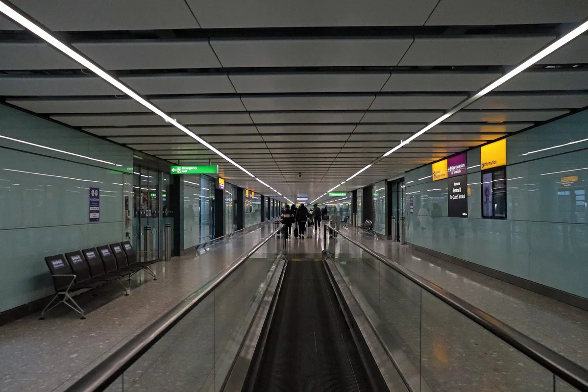 Lang ankomstkorridor med rullebånd på Heathrow Terminal 2, der reisende går mot passkontrollen