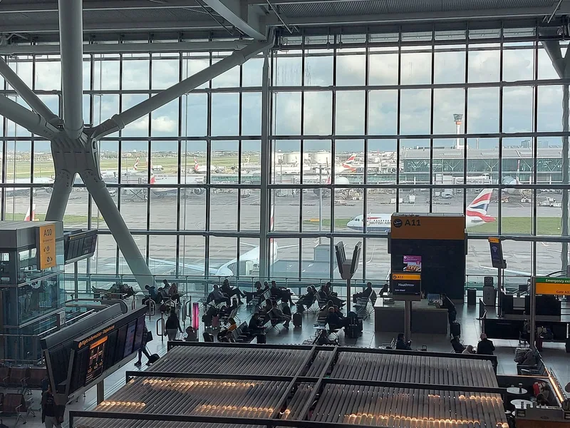 Avgangshallen på Heathrow Terminal 5 med ventende reisende og British Airways-fly bak glassveggen