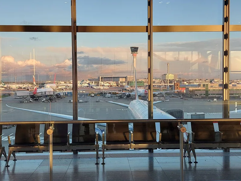 Tomme seter ved panoramavinduet på Heathrow Terminal 5, med fly og kontrolltårnet i solnedgang