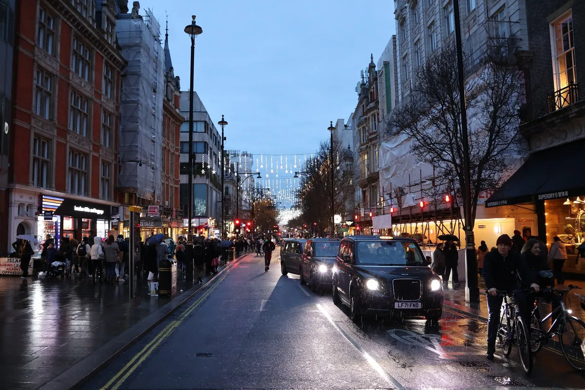 Oxford Street i skumringen med julebelysning, butikker og svarte drosjer på våt gate