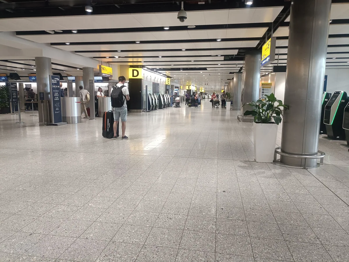 Avgangshallen i Terminal 3 på Heathrow med innsjekkingsautomater og en reisende med koffert