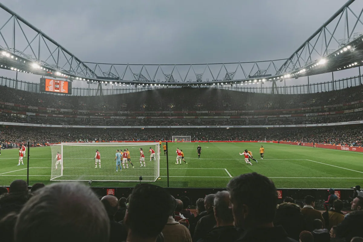 Fotballkamp under flomlys på Emirates Stadium, sett fra tribunen bak publikum like ved mållinjen