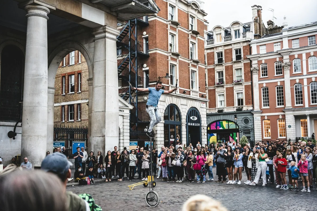 Gatekunstner på en høy enhjulssykkel foran et stort publikum på torget i Covent Garden