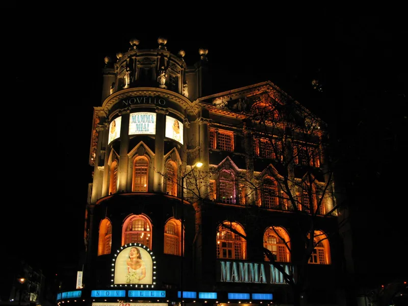 Novello Theatre i Aldwych opplyst om kvelden, med Novello-skiltet og lysende plakater for Mamma Mia! på fasaden