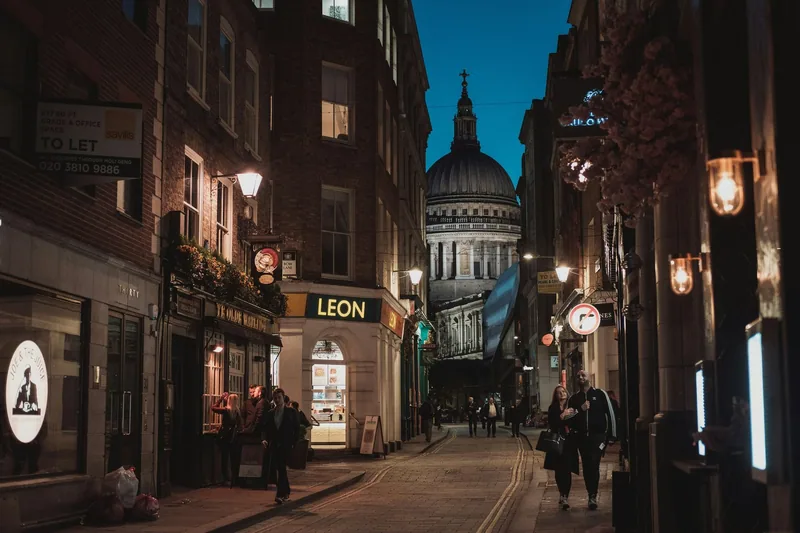 Smal gate i City of London om kvelden, med en Leon-kafé og kuppelen på St. Paul’s Cathedral i enden