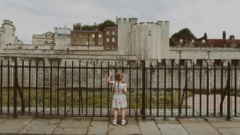 Liten jente ved gjerdet utenfor Tower of London, sett bakfra mot de gamle festningsmurene