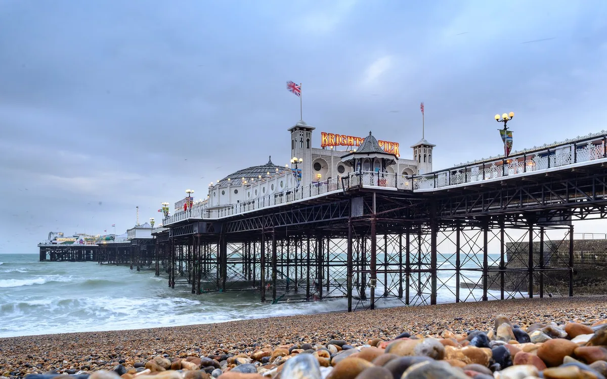 Brighton Palace Pier sett fra rullesteinstranden en grå dag, med bølger som slår inn under piren
