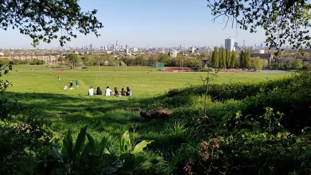 Utsikt fra Parliament Hill en solrik vårdag, med folk i gresset og Londons skyline i det fjerne