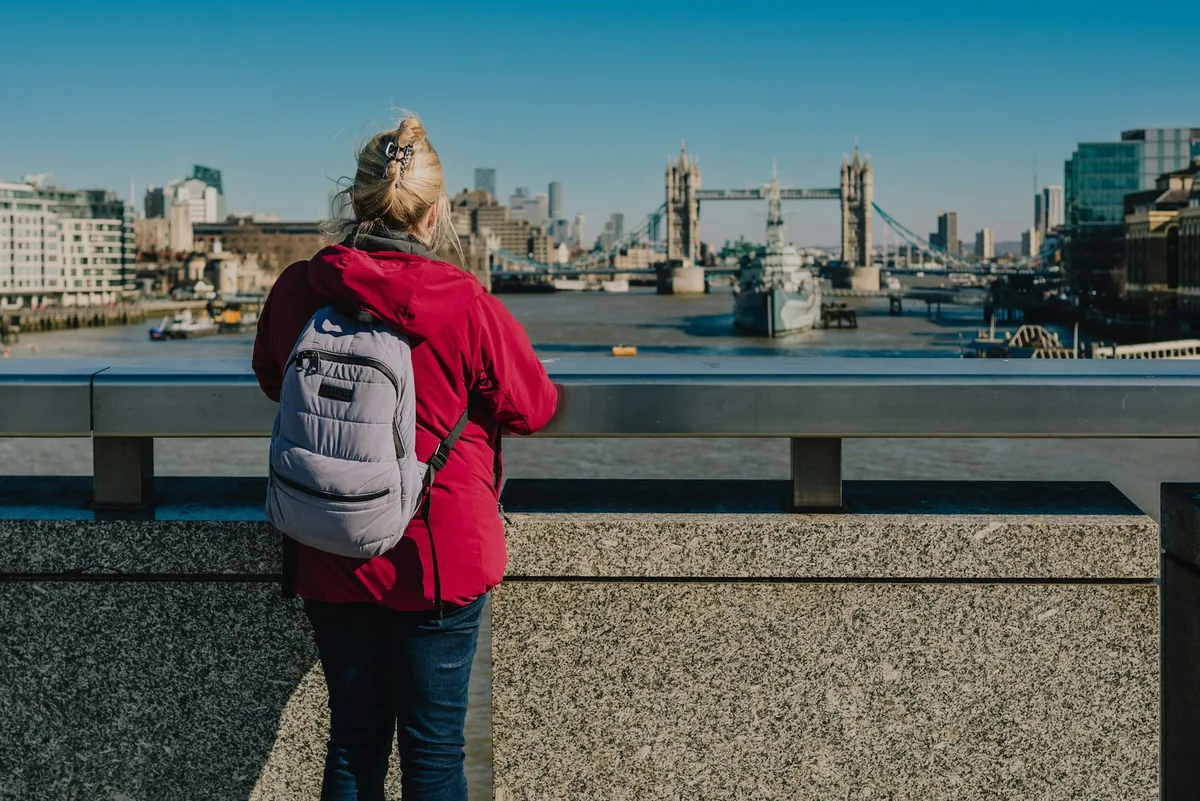 Kvinne med ryggsekk på London Bridge ser utover Themsen mot HMS Belfast og Tower Bridge