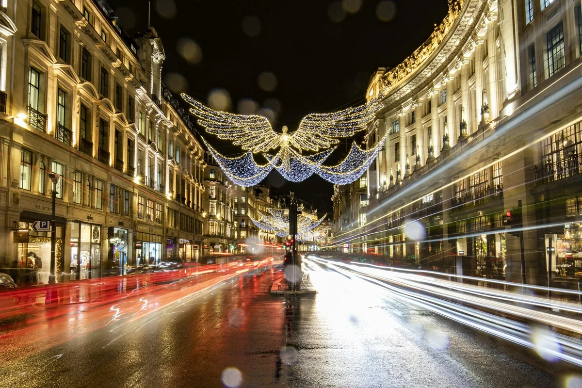 Julebelysning med lysende engler over Regent Street om kvelden, med lysstriper fra trafikken på våt gate