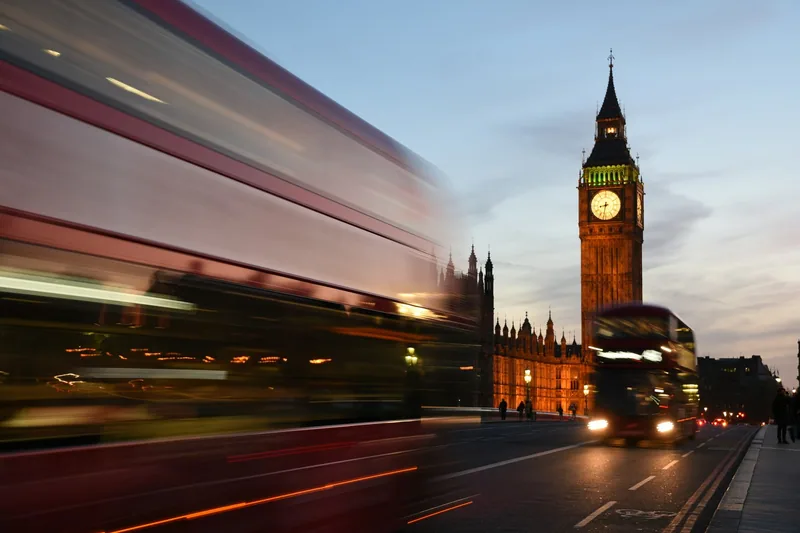 Rød dobbeltdekker i fart forbi Big Ben i kveldslys, uskarp av bevegelsen