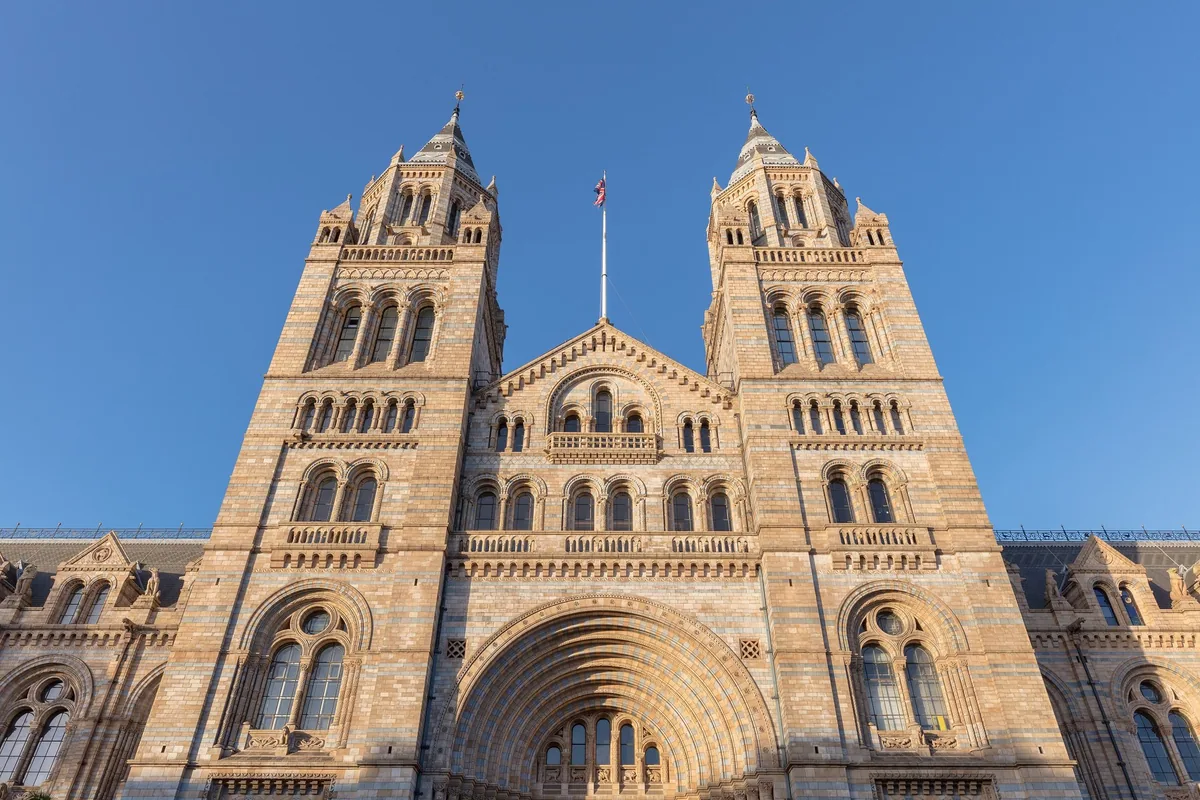 Hovedfasaden til Natural History Museum i South Kensington med de to tårnene i lavt sollys mot blå himmel