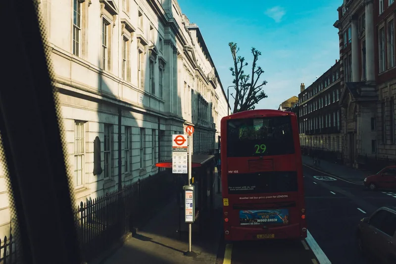 Rød dobbeltdekker ved et busstopp med TfL-skilt i en rolig gate, sett fra en annen buss