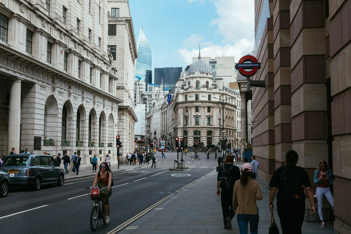 Fotgjengere og en syklist i en gate i City of London, med undergrunnsskilt, klassiske fasader og skyskrapere bak