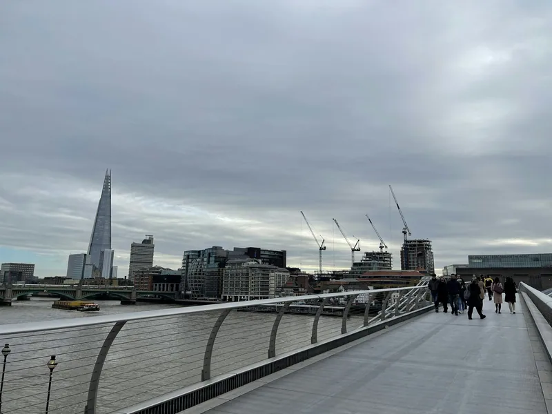 Fotgjengere på Millennium Bridge med The Shard og Tate Modern på sørbredden en gråværsdag