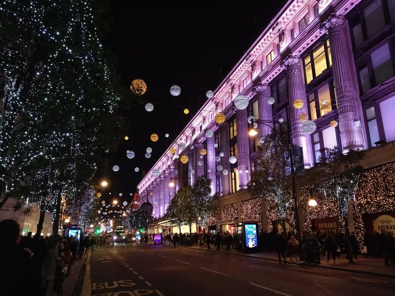 Selfridges i Oxford Street opplyst i lilla en kveld i julesesongen, med lyskuler over gaten og handlende på fortauet