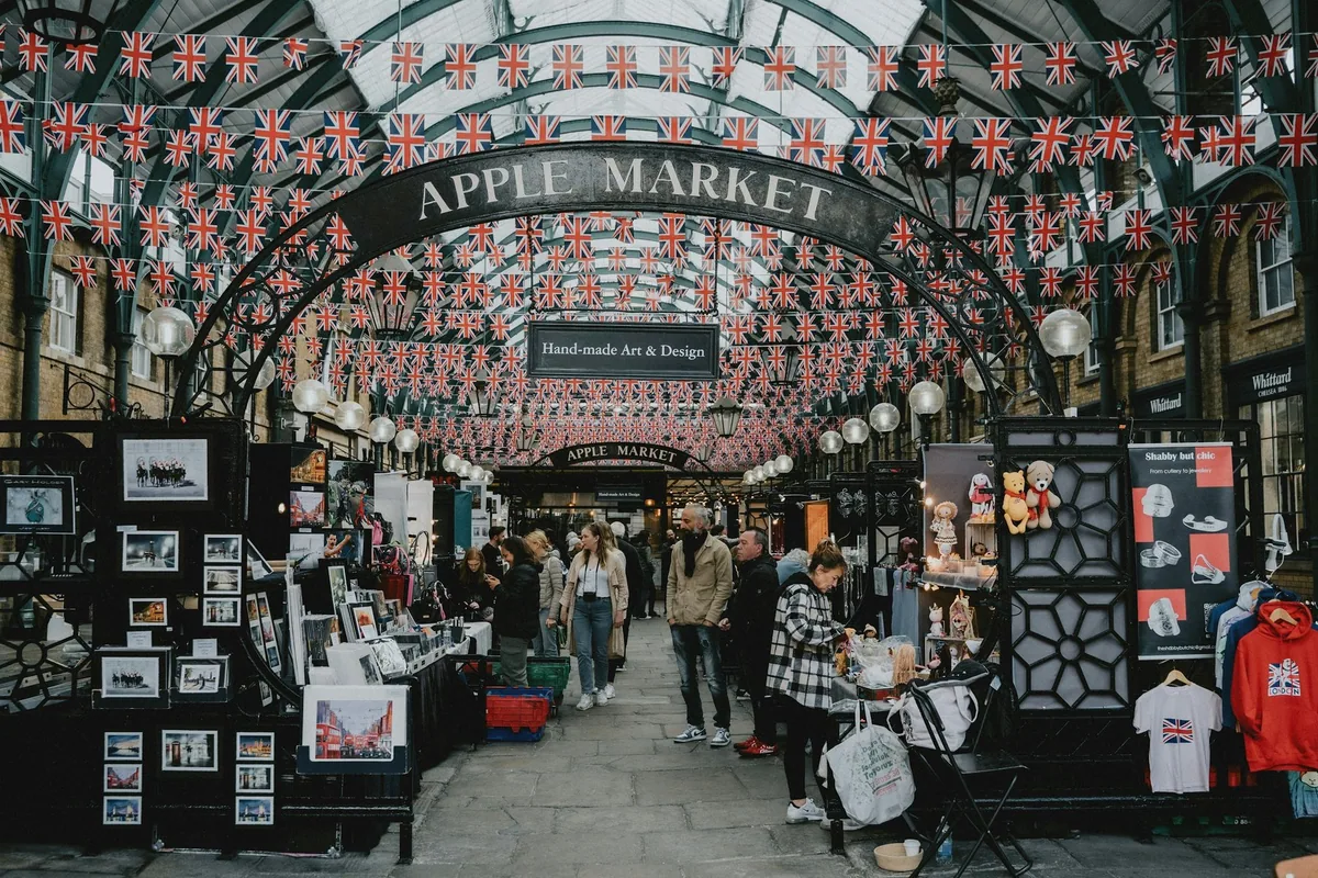 Boder med kunst og suvenirer i Apple Market i Covent Garden, under et glasstak pyntet med hundrevis av britiske flagg