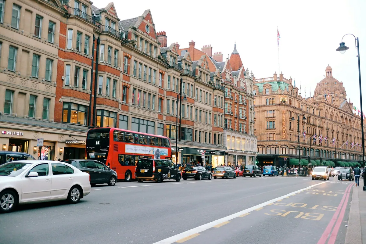 Varehuset Harrods med kuppeltak i enden av en travel gate i Knightsbridge, med rød buss og taxier