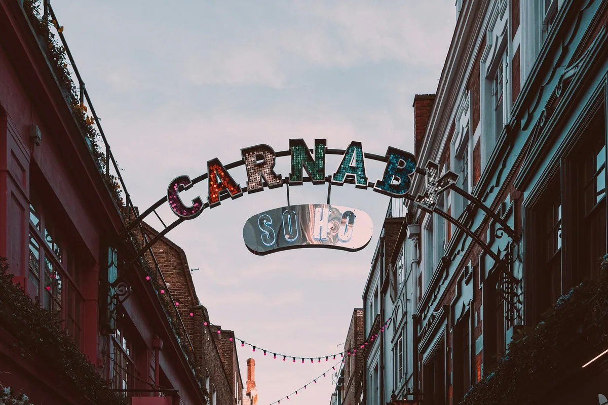 Buen med «Carnaby» og «Soho» over gaten mellom murbygninger, med lyslenker under en blek kveldshimmel