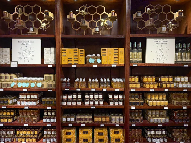 Hyller med honningglass, gule esker og bikubepynt i honningavdelingen hos Fortnum & Mason
