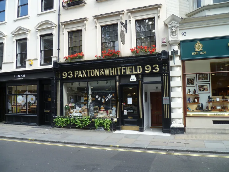 Ostebutikken Paxton & Whitfield i nr. 93 Jermyn Street, med gullbokstaver på sort fasade og en skobutikk ved siden av