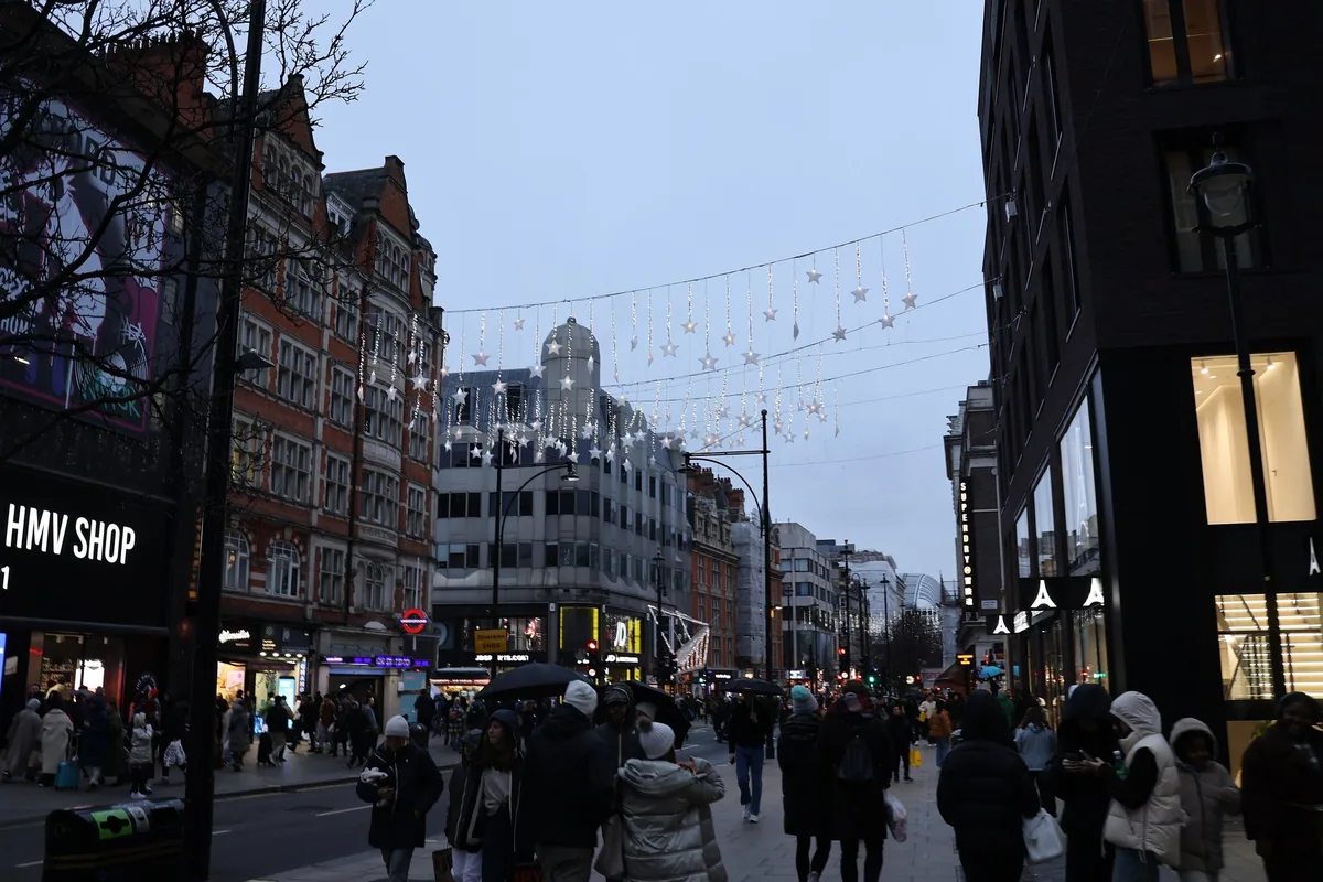 Handlende med poser og paraplyer på fortauet i Oxford Street en grå januardag, under stjernebelysning