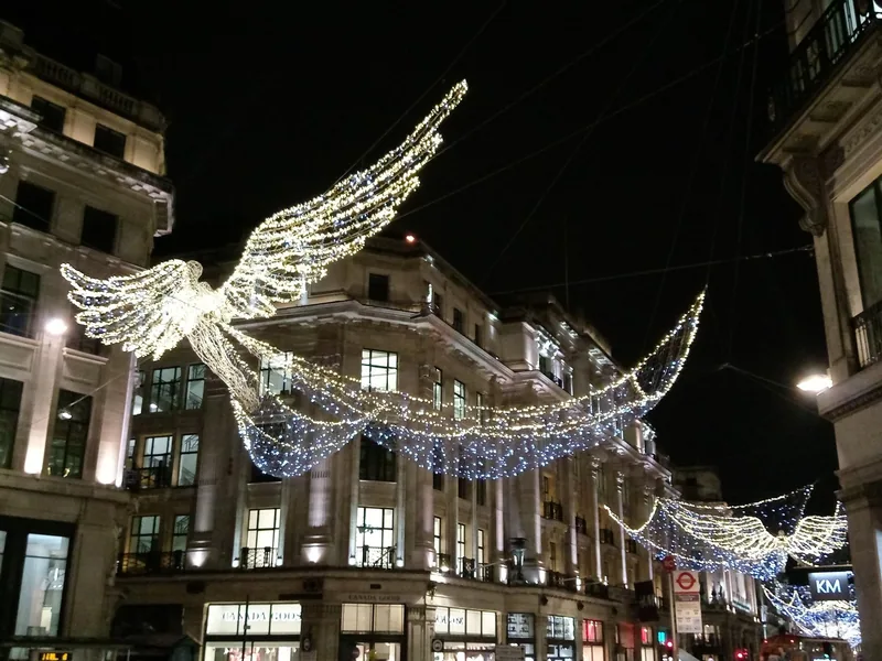Opplyste engler i julebelysningen henger over butikkene i Regent Street en vinterkveld