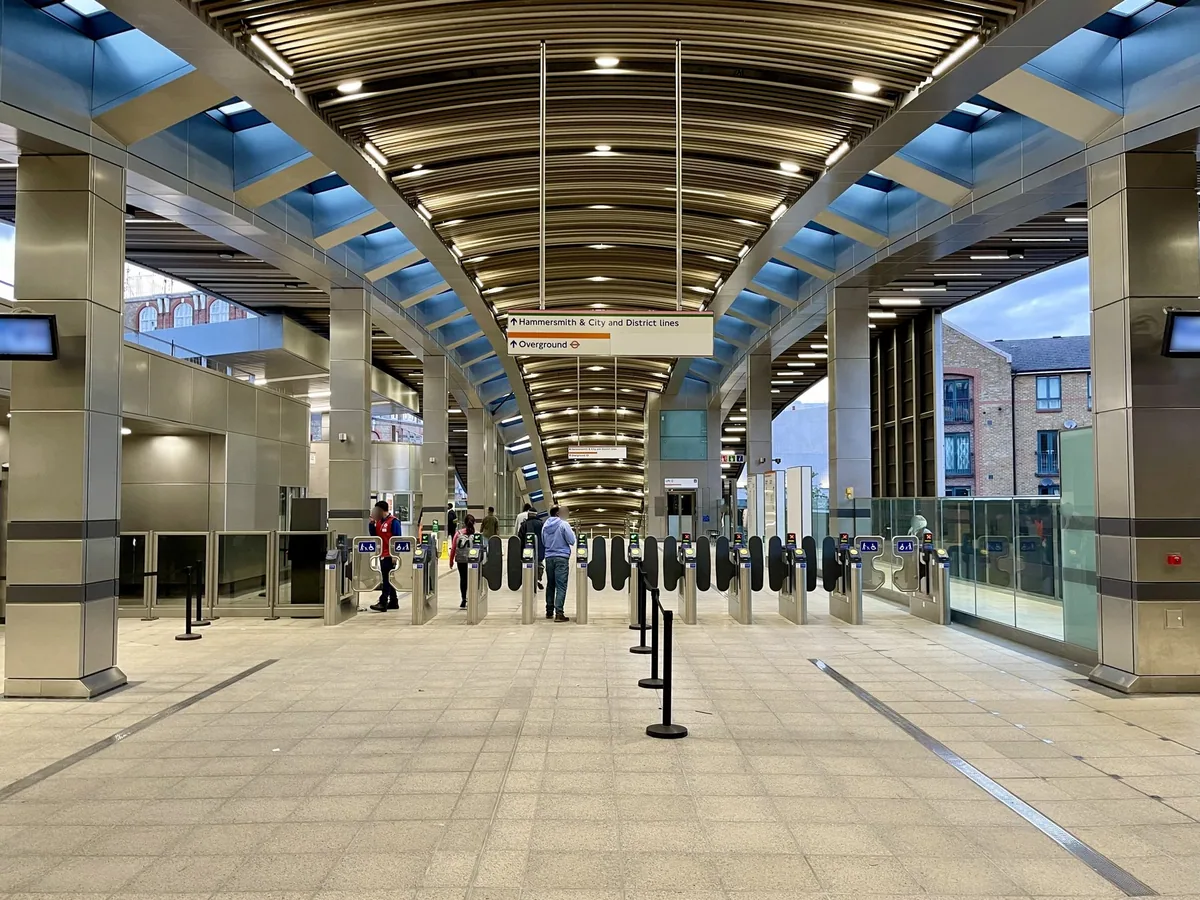 Billettsperrer i billetthallen på Whitechapel stasjon under et buet tak med skilt mot Overground