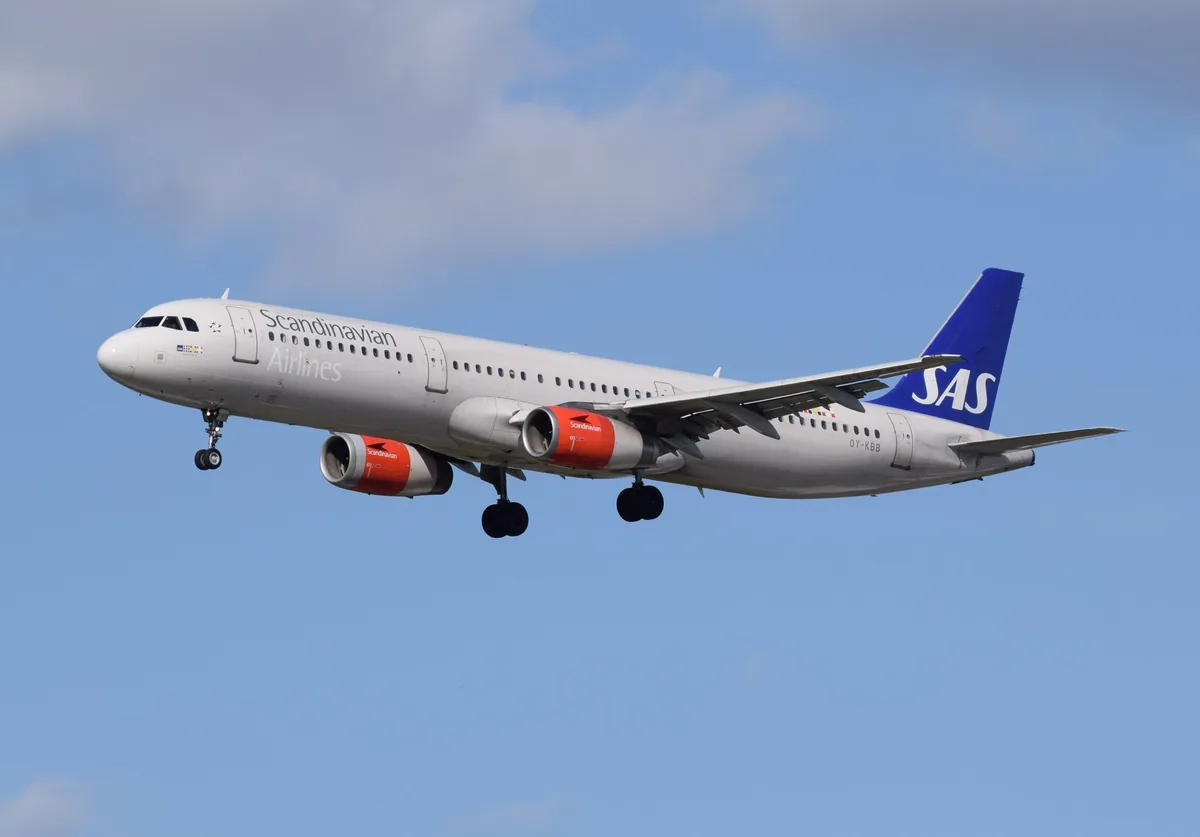 Et fly fra SAS med understellet ute på innflyging til Heathrow under blå himmel