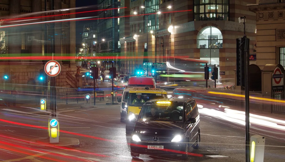 Kveldstrafikk med drosjer og lysspor fra busser i krysset ved Bank i City of London