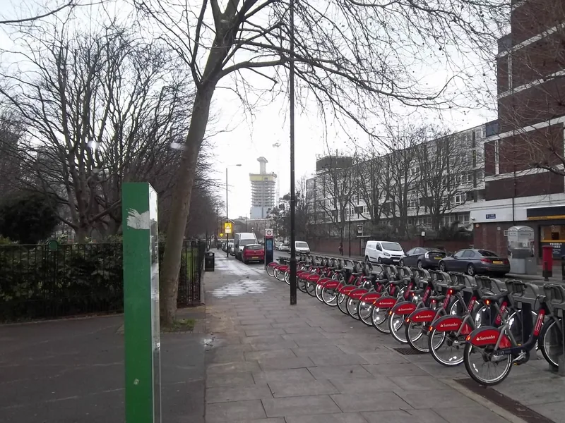 En lang rekke røde Santander-bysykler i stativet langs et fortau ved Manchester Road en grå vinterdag