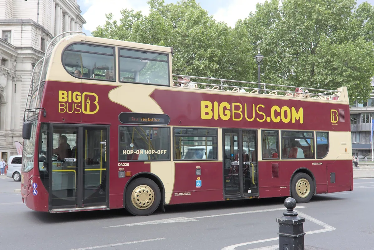 Vinrød og kremgul hop-on hop-off-buss med åpent øvre dekk i Westminster