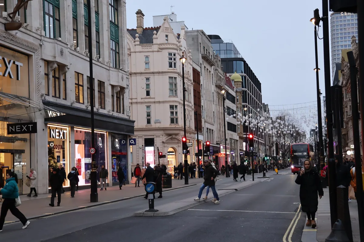 Butikkfasaden til Next på Oxford Street en grå vinterdag, med julelys over gata og en rød buss i det fjerne